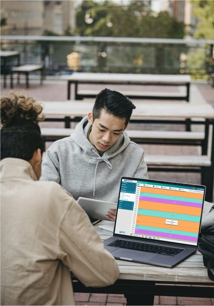 Outdoor business collaboration with Infinity Media software on display, showcasing a professional in a casual hoodie analyzing real-time broadcast scheduling data on a laptop.