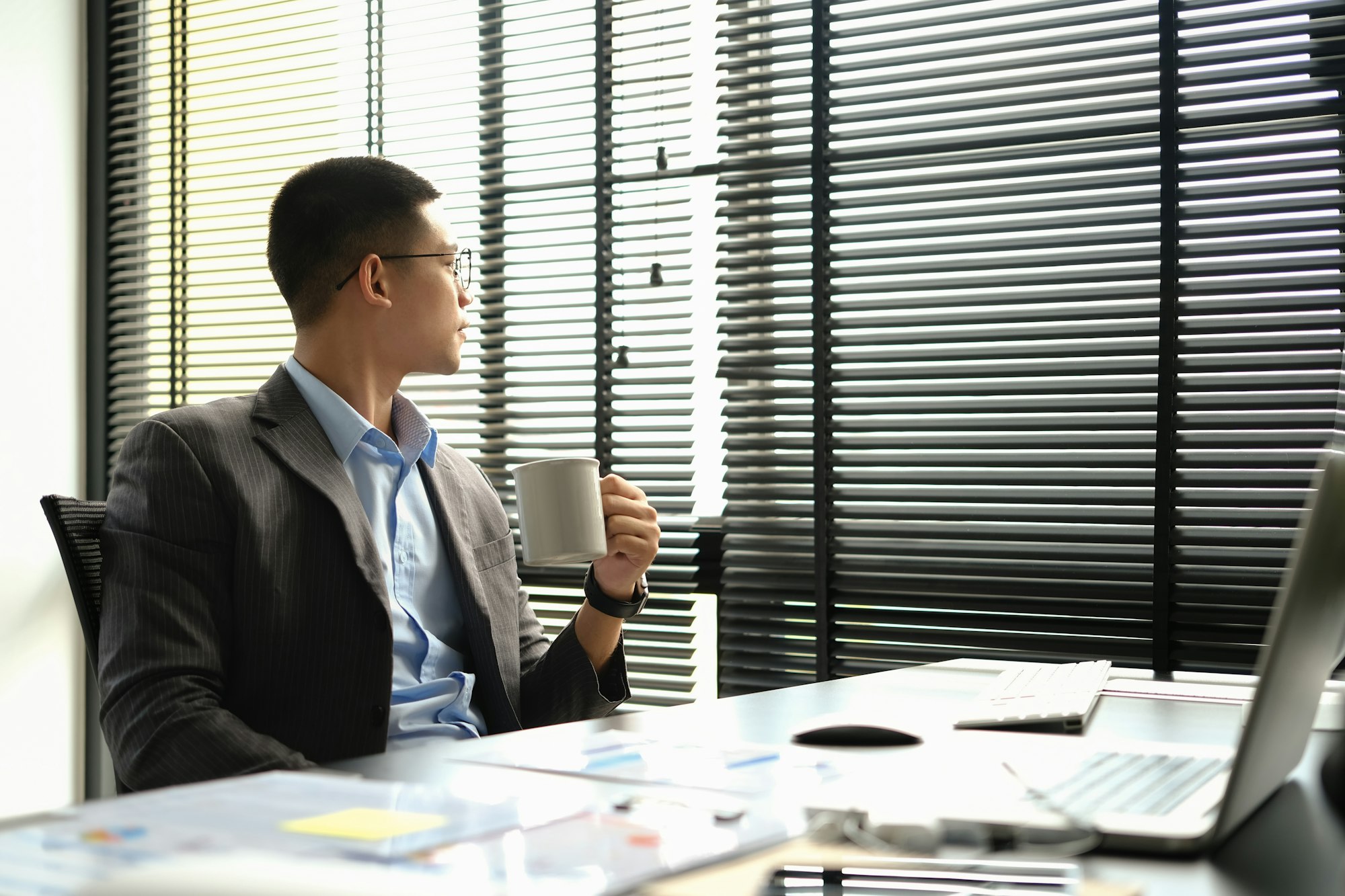 Thoughtful businessman sitting at office desk and looking away, thinking of future career vision.